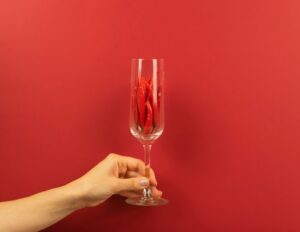 A woman’s hand holds a wine glass full of red hot pepper om a