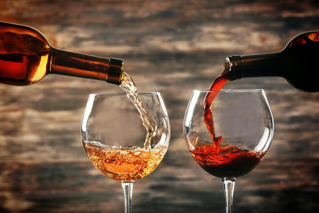 A bottle of white wine filling up a glass alongside a glass being filled from a bottle of red wine.