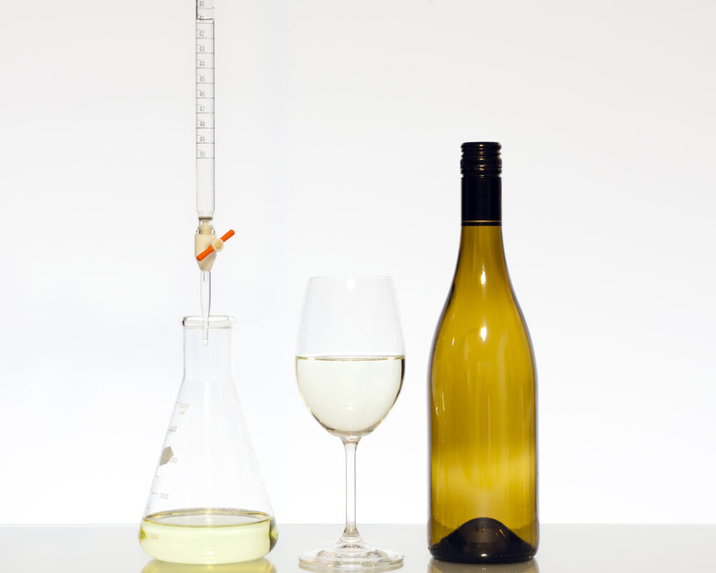 A bottle and glass of white wine next to a flask for acid titration.