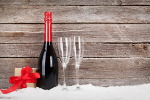 Bottle of red wine in the snow, next to two empty glasses and a small wrapped gift box.