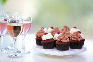 Photo of glasses of rosé wine next to cupcakes with pink and white frosting.