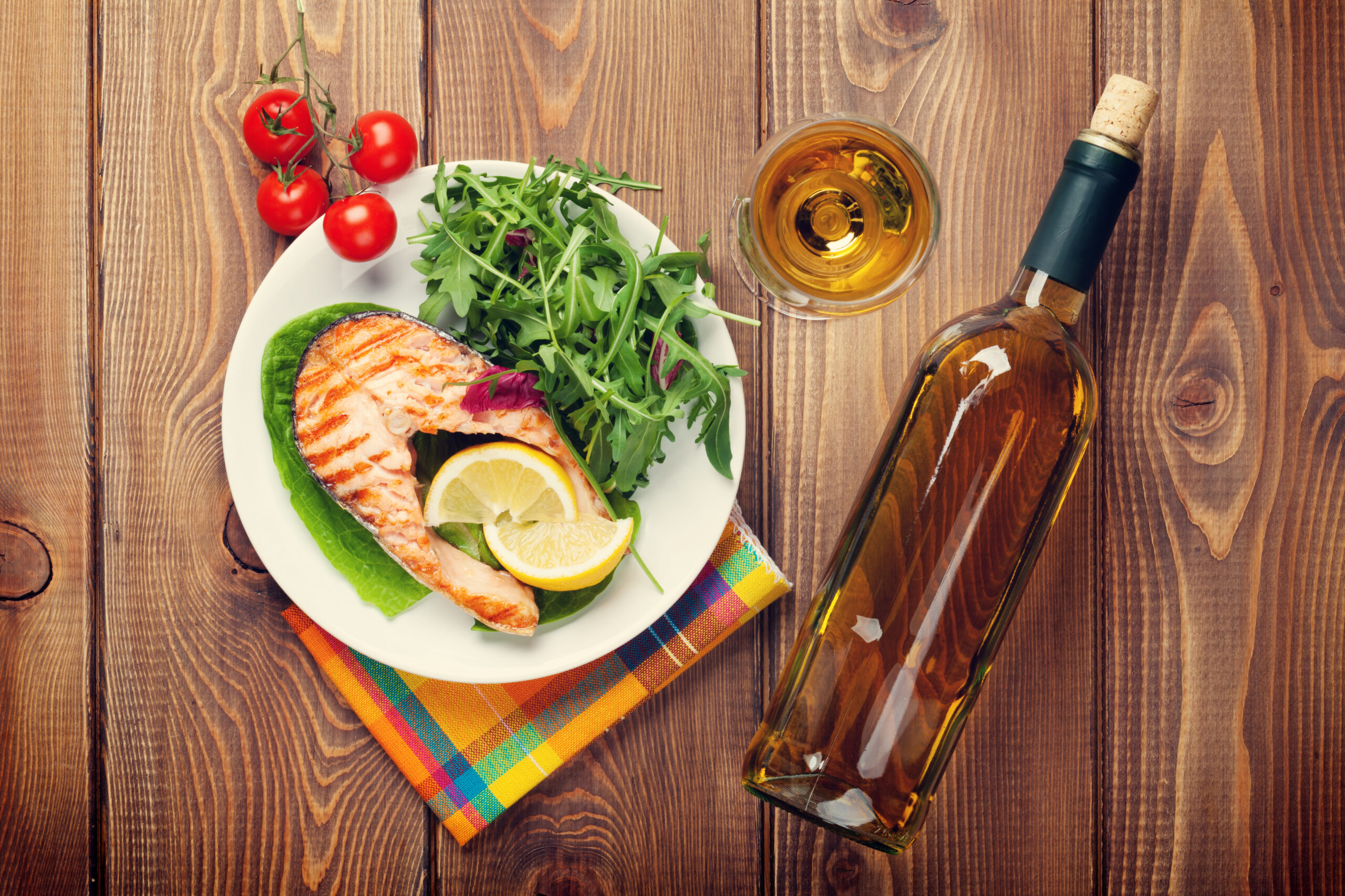 A plate with salmon and arugula salad next to a bottle of white wine on a table.